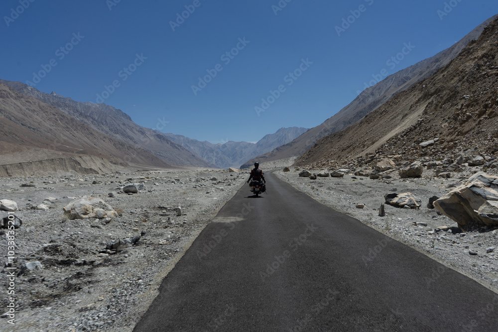Motorcyclist riding on a remote mountain road surrounded by rugged terrain Motorcyclist riding on a remote mountain road surrounded by rugged terrain