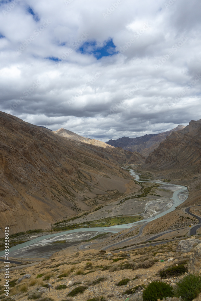 A winding river flowing through a mountainous valley under a cloudy sky A winding river flowing through a mountainous valley under a cloudy sky