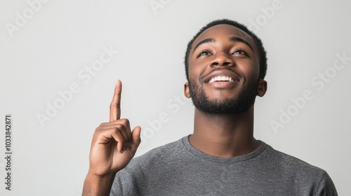 Black man with a gentle smile, wearing a gray shirt and pointing upwards as if showing something interesting, on a plain background