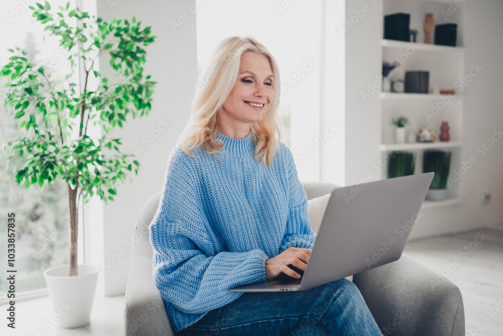 Naklejka premium Photo of pretty aged woman sit chair use laptop wear pullover free time modern apartment indoors