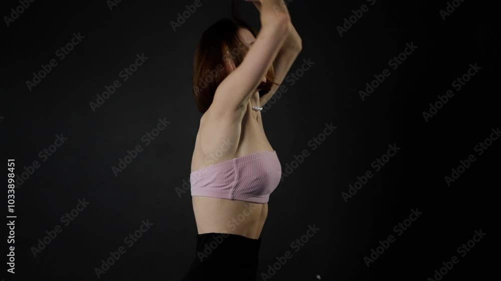 Young woman with a pearl necklace is performing a dance routine on a black background. She is wearing a pink tube top and black pants Young woman with a pearl necklace is performing a dance routine on a black background. She is wearing a pink tube top and black pants