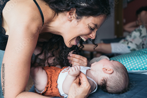 Tableau sur toile Happy mother playing with her baby lying on a bed