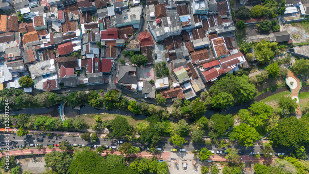 Fototapeta premium Overhead view showcases a dense residential area alongside a river, framed by trees and pathways
