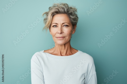 Portrait of a content woman in her 50s sporting a long-sleeved thermal undershirt in soft teal background