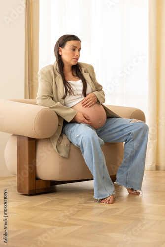 Stylish pregnant woman in the room on a chair. Concept of style and pregnancy.