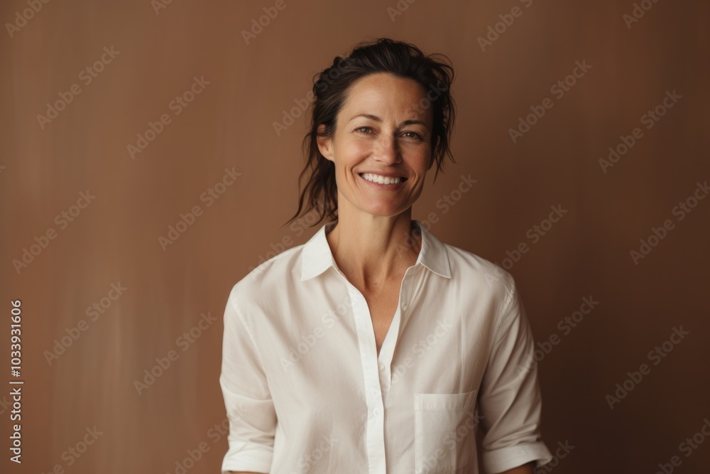 Portrait of a blissful woman in her 40s wearing a simple cotton shirt isolated on soft brown background Portrait of a blissful woman in her 40s wearing a simple cotton shirt isolated on soft brown background