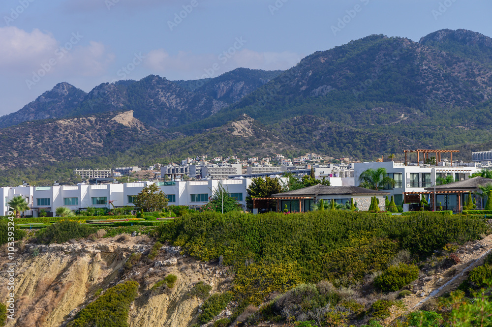 Luxurious hillside residences overlooking the vibrant coastal town beneath majestic mountains on a sunny day Luxurious hillside residences overlooking the vibrant coastal town beneath majestic mountains on a sunny day