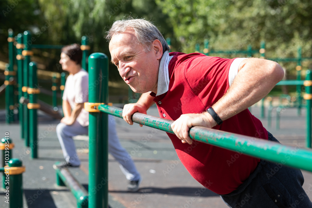 Fototapeta premium Elderly man doing exercises on a horizontal bar at an outdoor sports ground