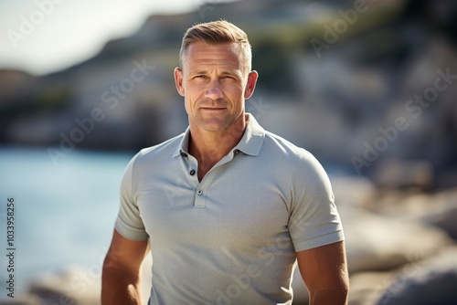 Portrait of a glad man in his 40s wearing a sporty polo shirt isolated on rocky shoreline background