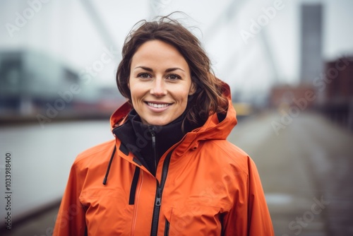 Portrait of a smiling woman in her 30s dressed in a water-resistant gilet in modern cityscape background