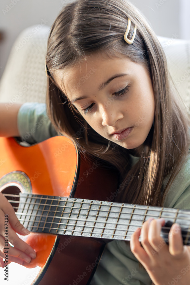 Fototapeta premium A cute girl plays the guitar. A little girl with a guitar.