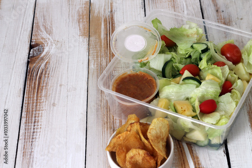 Healthy meal consisting of a fresh vegetable salad and crispy chips packed in a transparent box, served with creamy peanut sauce. Called Selada Bangkok.in Indonesia. Vibrant and colorful appearance. photo