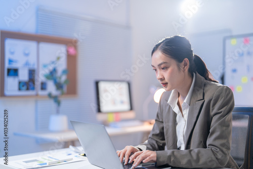 Young businesswoman is working late, concentrating on a project on her laptop in a modern office. The image suggests dedication, ambition, and the challenges of meeting deadlines