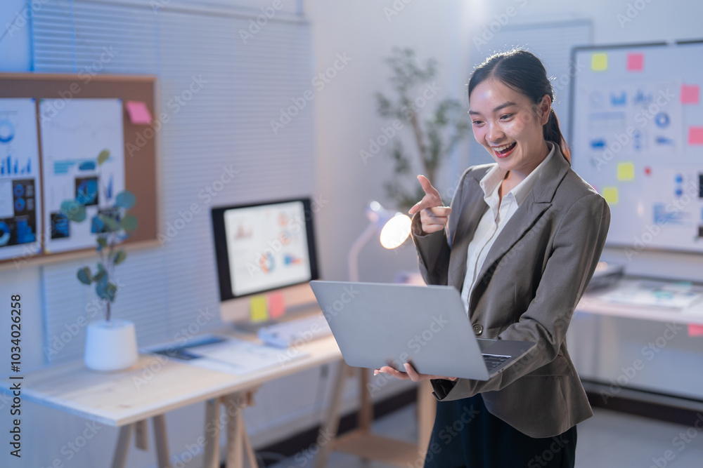 Young manager is smiling and pointing at her laptop screen while presenting a business plan during a video conference call Young manager is smiling and pointing at her laptop screen while presenting a business plan during a video conference call