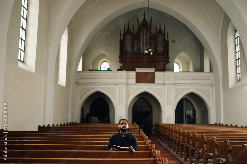 Fototapeta premium Priest sitting in church pew reading bible