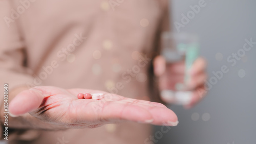 Supplements, Persons hand holds two capsules and tablet, accompanied by glass of water, symbolizing daily medication routine and health management practices photo