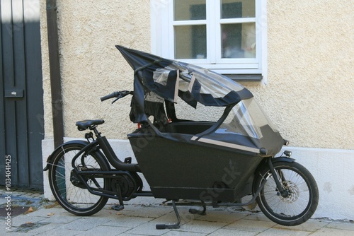 Schwarzes Lastenrad, das auf einem Gehweg vor einer Hauswand geparkt ist.