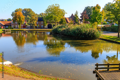 Fishing pond in public park, reflection on water surface, trees and cityscape in background, sunny autumn day in Wijnandsrade, South Limburg, Netherlands