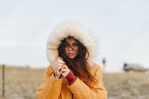 Woman in yellow jacket and fur coat standing in field on fashionable autumn trip to nature