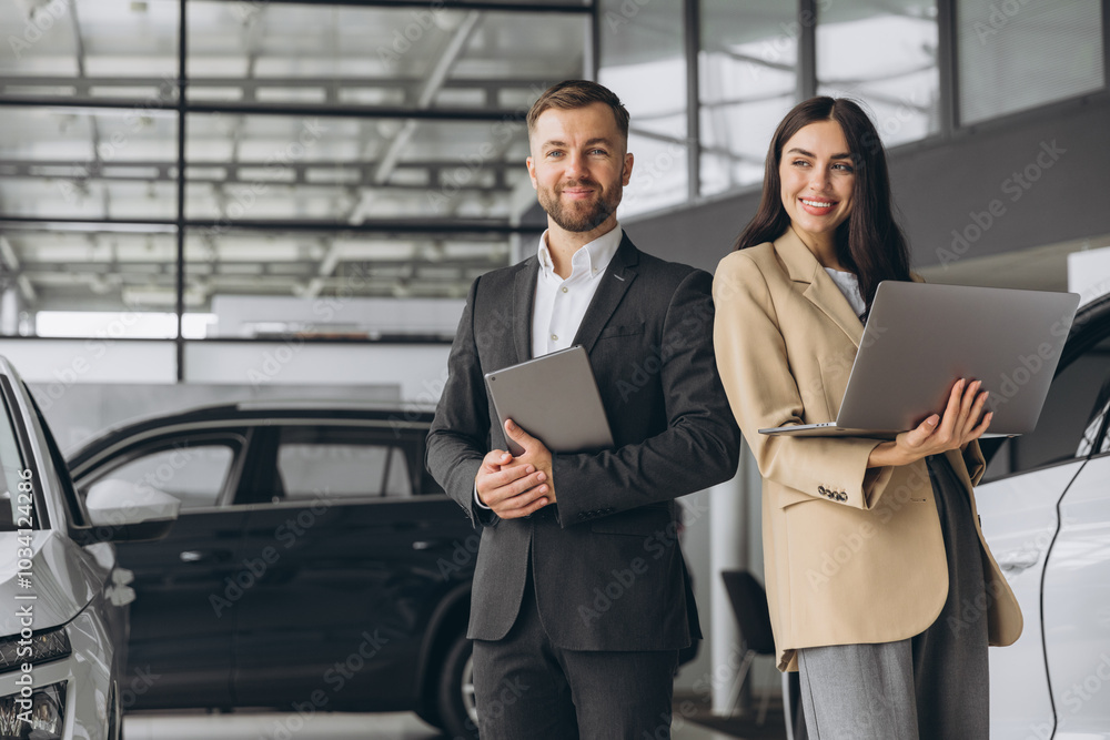 Super sales team in dealership, two consultants or managers in elegant suits with laptop and tablet in arms in car dealership Super sales team in dealership, two consultants or managers in elegant suits with laptop and tablet in arms in car dealership