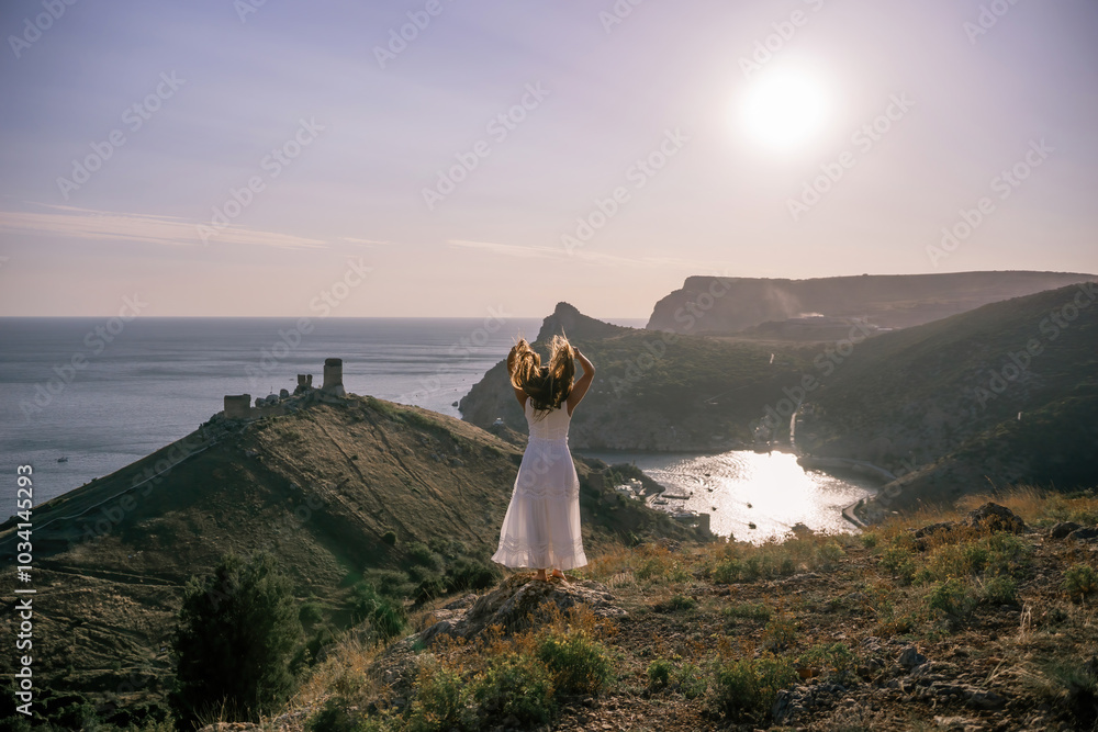 woman stands on a hill overlooking the ocean, her arms raised in the air. Concept of freedom and joy, as if the woman is celebrating a moment of happiness or accomplishment. woman stands on a hill overlooking the ocean, her arms raised in the air. Concept of freedom and joy, as if the woman is celebrating a moment of happiness or accomplishment.