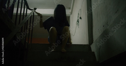 Horror scene of a mysterious Scary Asian ghost woman creepy have hair covering the face sitting on staircase at abandoned house with background dark scene movie at night, festival Halloween concept