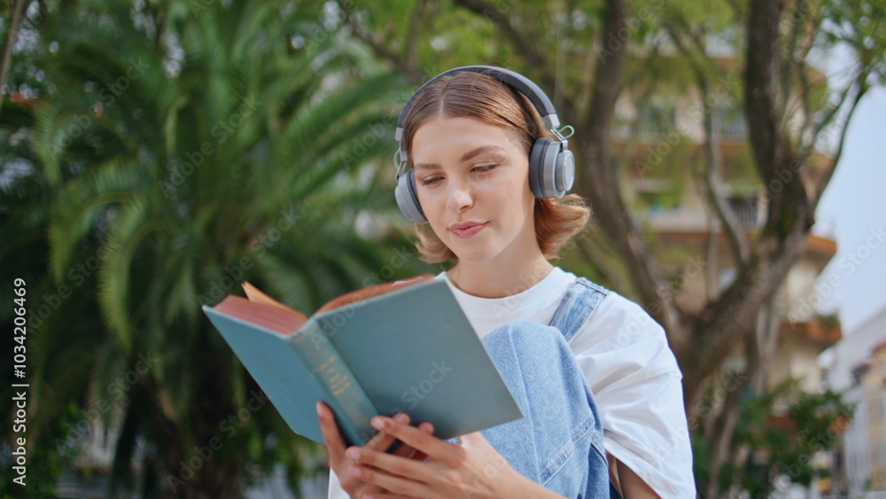Peaceful girl reading literature in headphones sitting calmly in park closeup. Peaceful girl reading literature in headphones sitting calmly in park closeup.