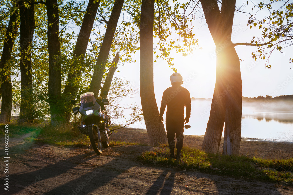 A motorcyclist is enjoying the last warm days of autumn. back view. Sun rays of sunset. the road near the lake. A biker in special clothes and a helmet. Silhouette of a motorcycle