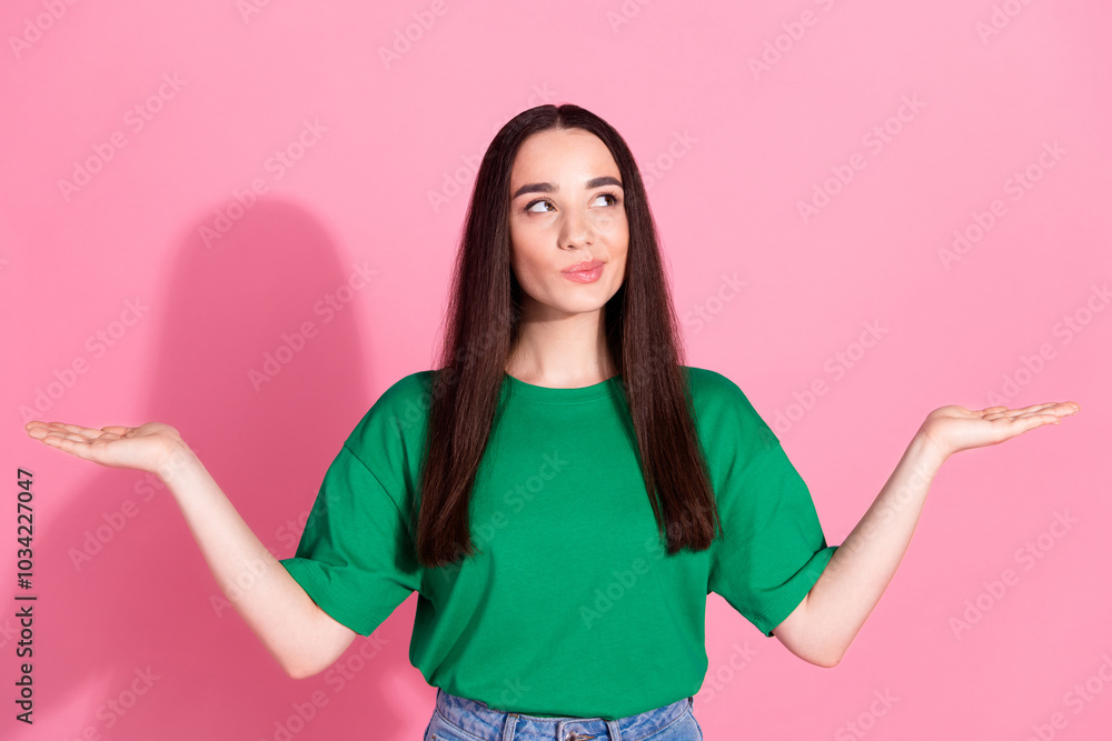 Photo of doubtful pretty lady dressed green t-shirt comparing arms empty space isolated pink color background Photo of doubtful pretty lady dressed green t-shirt comparing arms empty space isolated pink color background