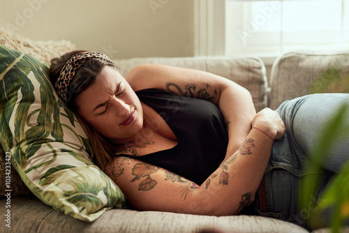 Photos Sick, woman and stomach pain on sofa in home with uncomfortable ache, pms bloating and period cramps