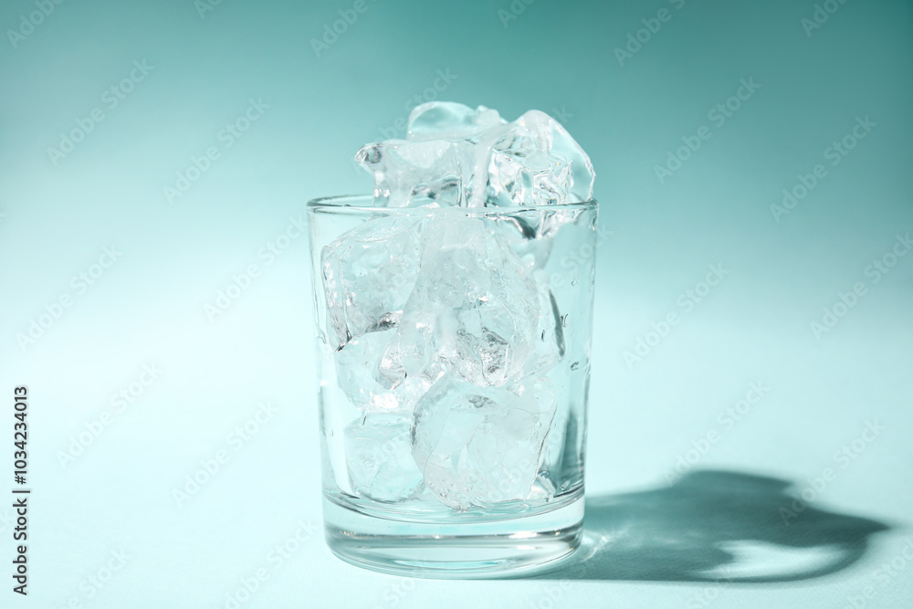 One glass with ice for refreshing drink on turquoise background, closeup