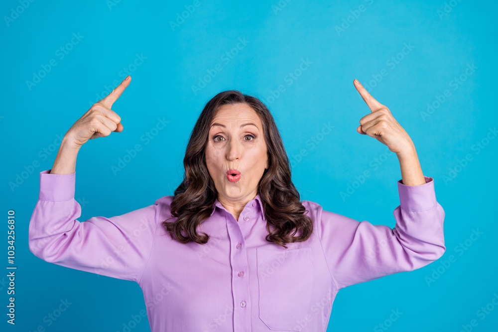Photo of adorable excited woman wear violet shirt pointing two fingers up empty space isolated blue color background Photo of adorable excited woman wear violet shirt pointing two fingers up empty space isolated blue color background