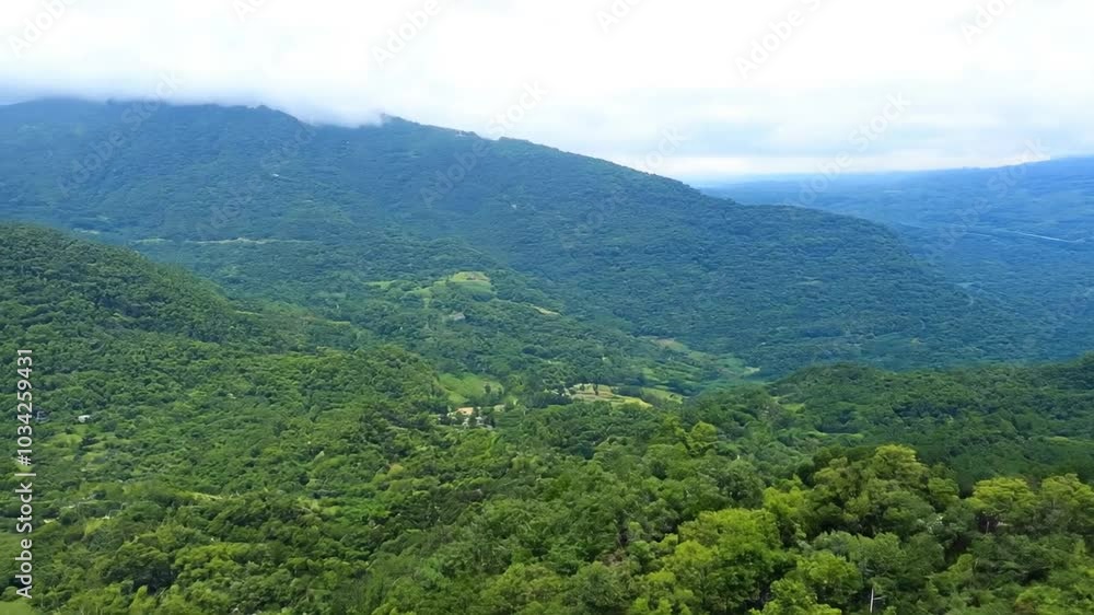 Clouds drift over a mountain range adorned with lush green forests, creating a serene and picturesque landscape Clouds drift over a mountain range adorned with lush green forests, creating a serene and picturesque landscape