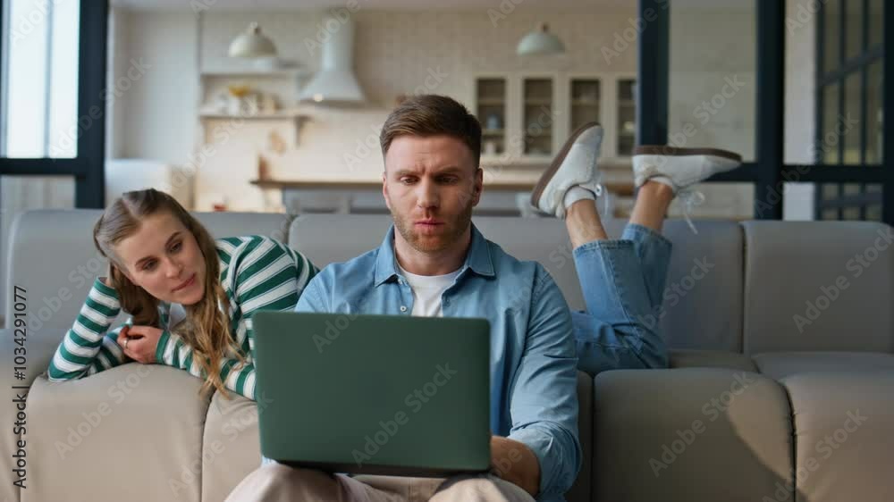 Focused boyfriend working laptop girlfriend leaning at sofa. Man solving tasks Focused boyfriend working laptop girlfriend leaning at sofa. Man solving tasks