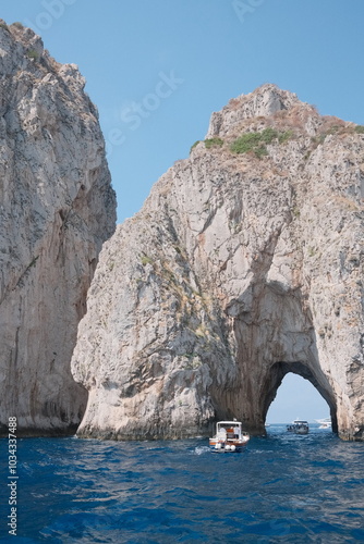 Wallpaper Mural A boat sails through the iconic rock arch in Capri, Italy, with towering cliffs and crystal blue waters under a bright sky, showcasing the island’s dramatic coastal beauty. Torontodigital.ca