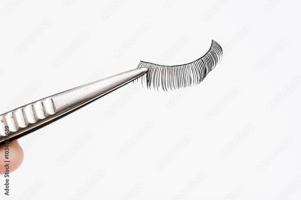 False eyelashes holded by tweezers on white background. Cosmetic products for beauty and makeup artist. Closeup. False eyelashes holded by tweezers on white background. Cosmetic products for beauty and makeup artist. Closeup.