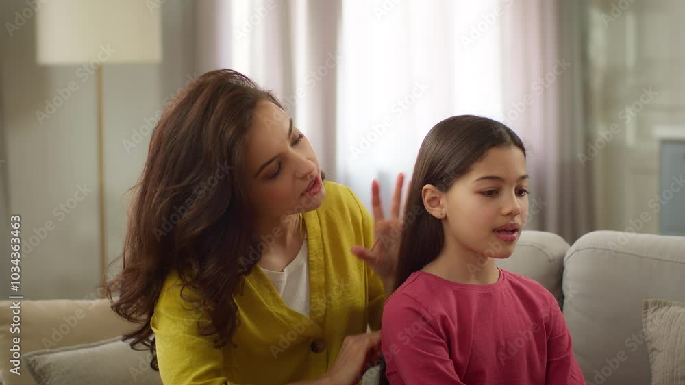 Smiling friendly family Caucasian sisters woman female mother sister babysitter combing brushing hair make hairstyle coiffure talking with little girl sibling child kid daughter sit living room home Smiling friendly family Caucasian sisters woman female mother sister babysitter combing brushing hair make hairstyle coiffure talking with little girl sibling child kid daughter sit living room home