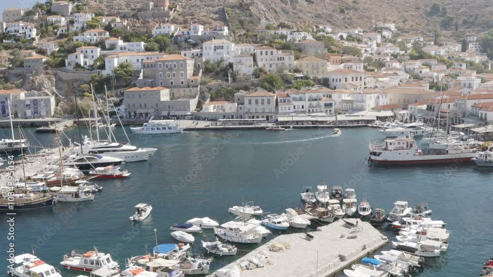 A picturesque daytime view of Hydra port in summer, featuring a handheld shot from a high point, capturing small boats entering and leaving the harbor. A picturesque daytime view of Hydra port in summer, featuring a handheld shot from a high point, capturing small boats entering and leaving the harbor.