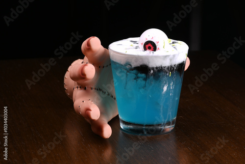 hand picking up drink blue curaçao cocktail with decorative eye and ginger spuma at halloween party photo