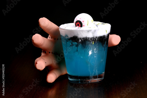 hand picking up drink blue curaçao cocktail with decorative eye and ginger spuma at halloween party with blurred background photo