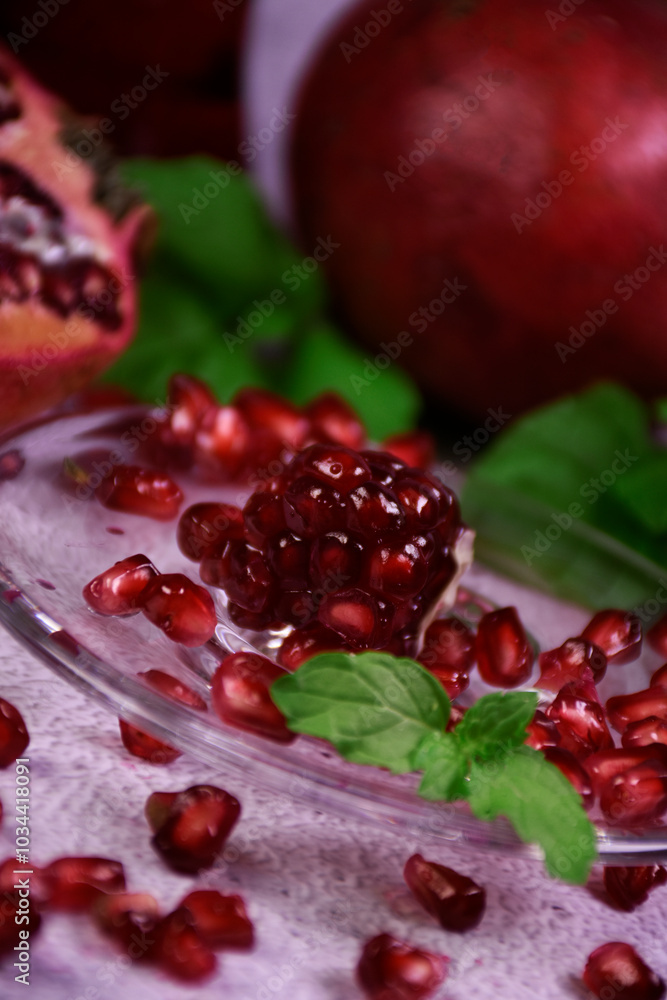 Red pomegranate on a gray background. Whole and pieces. Ripe pomegranate seeds on a glass plate. All mint leaves. Red pomegranate on a gray background. Whole and pieces. Ripe pomegranate seeds on a glass plate. All mint leaves.