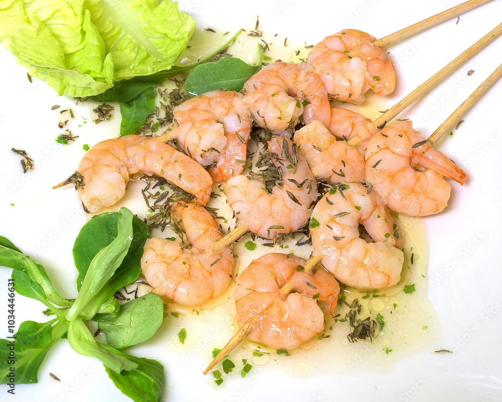 Garlic prawn skewer with olive oil on a white plate with lettuce leaves and lamb's lettuce Garlic prawn skewer with olive oil on a white plate with lettuce leaves and lamb's lettuce