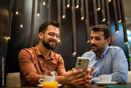 Two colleagues hanging out at the coffee shop. Working together on phone. photo