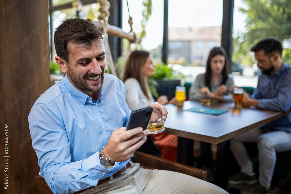 Businessman using his phone in the restaurant. Smiling and drinking beer. Businessman using his phone in the restaurant. Smiling and drinking beer.