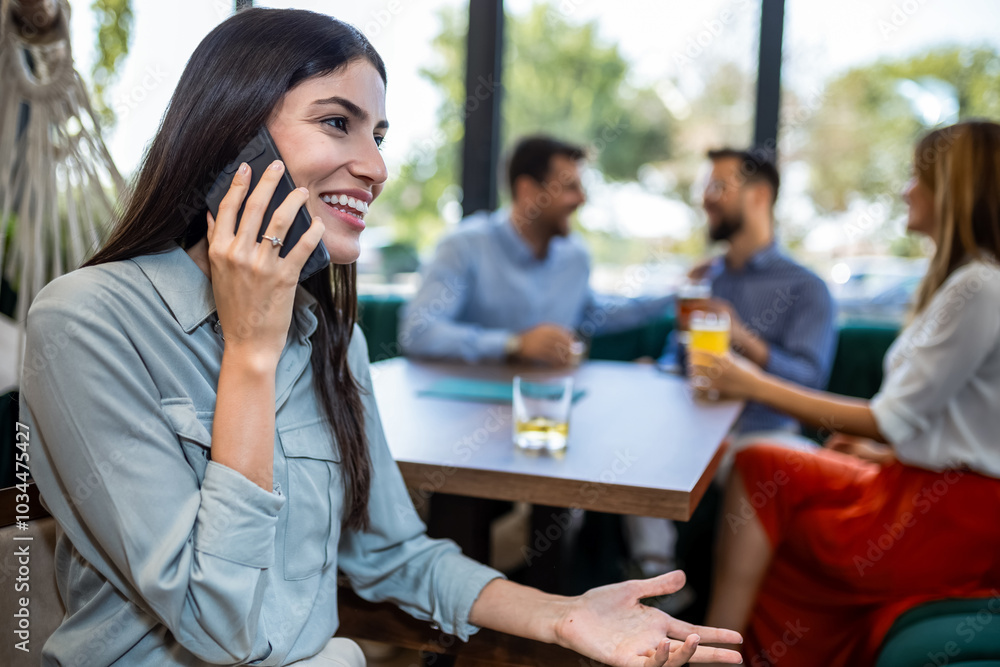 Woman talking on her phone in the restaurant while her friends are in the background. Woman talking on her phone in the restaurant while her friends are in the background.