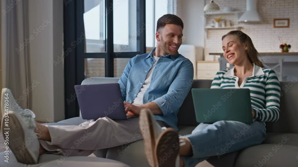 Focused couple working laptops at living room interior. Happy man looking woman Focused couple working laptops at living room interior. Happy man looking woman