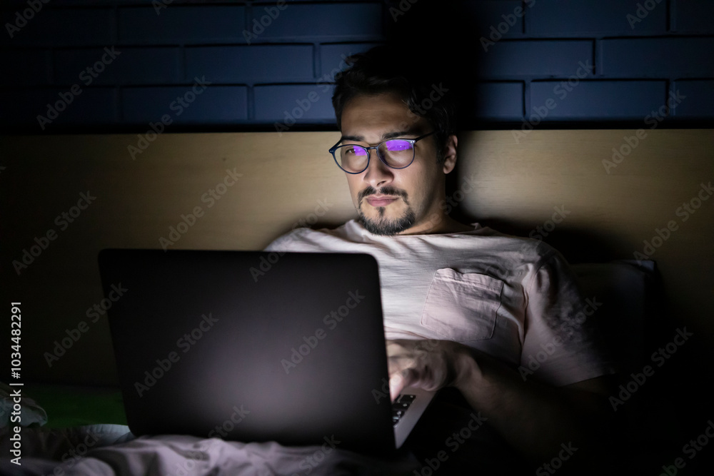 Concentrated man working on laptop in bed at night Concentrated man working on laptop in bed at night