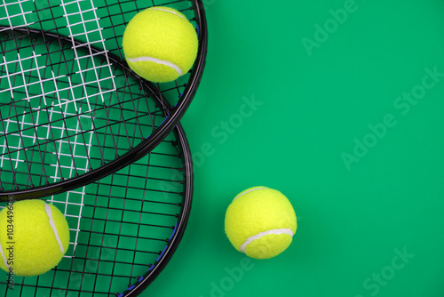 Top view on a green background, two tennis rackets for lawn tennis are lying on the side, yellow tennis balls with a place for text on the side are on top of them. High quality photo