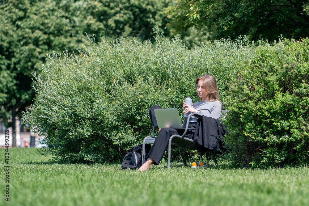Focused woman using laptop relaxed sitting barefoot on lawn enjoys opportunity to work or study remotely on fresh air. Interested female looking to screen portable computer outdoor surround by plants. Focused woman using laptop relaxed sitting barefoot on lawn enjoys opportunity to work or study remotely on fresh air. Interested female looking to screen portable computer outdoor surround by plants.