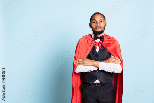 African american doorman posing in a superhero red mantle in studio, acting as a hero and savior for the clients. Happy confident bellhop with a superhuman cape, professionalism. photo